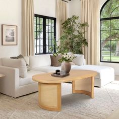 a living room filled with white furniture and large window covered in drapes on the windowsill