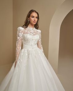 a woman in a white wedding dress with long sleeves and flowers on the skirt is posing