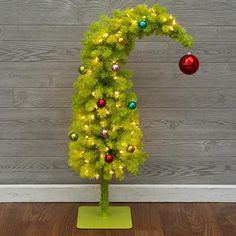 a green christmas tree with ornaments on it in front of a wooden wall and floor