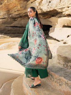 a woman standing on top of a rock next to the ocean wearing a green dress