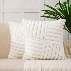 two white pillows sitting on top of a couch next to a plant