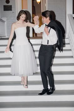 a man in a tuxedo and a woman in a white dress dance on steps