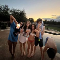 four young women standing next to each other in front of a swimming pool at sunset