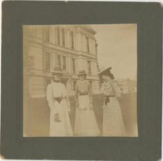 an old photo of three women standing in front of a building with two hats on