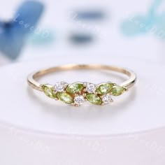 three stone ring with green and white stones on the side, sitting on top of a table