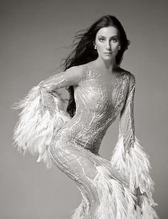 a woman in a silver dress with feathers on her arms and legs, posing for the camera