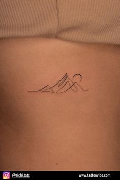 a woman's stomach with a mountain tattoo on her left side ribcage