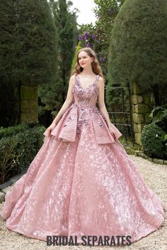 a woman wearing a pink dress standing in the middle of a gravel area with trees and bushes behind her