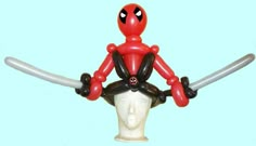 a red and black toy with two swords in it's hands, sitting on top of a white mannequin head