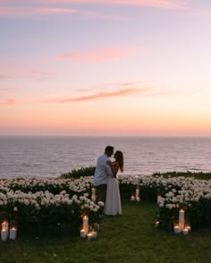 a bride and groom standing in front of flowers at sunset