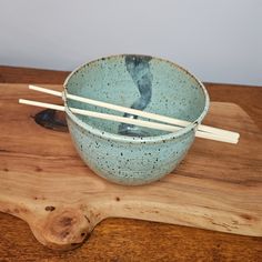 a bowl with chopsticks in it sitting on top of a wooden table next to a cutting board