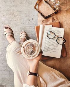 a woman with her feet up on a table next to an open book and reading glasses