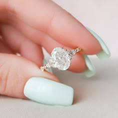 a woman's hand holding a diamond ring on top of her finger with white nail polish