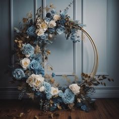 a wreath with blue flowers and greenery on a wooden floor in front of a wall