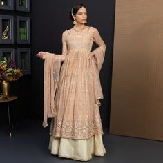 Nadia shines like a dream in the dusty peach hue of its chiffon fabric. The flared gown is a canvas of intricate embroidery, featuring sequins, tilla, and panni work. Adorned with a sequin edge finish, the squared neck is a regal addition to the long fitted sheer sleeves. Cotton silk lining embraces the body, while the deep back accentuates it with its dangling tassels. On the bottom, the lehnga sports a light gold raw silk fabric and pleated folds, finished off with a tilla braid edge. Inside, cotton lining feels like a soothing embrace. In perfect harmony, the chiffon dupatta boasts a thread, sequin, and panni embroidery, complemented by a tilla braid edge finish. Nadia is a piece of art that will make you shine bright like a star. Top: Color: Dusty Peach    Fabric: Chiffon  Flared gown Peach Anarkali Floor-length Dress, Peach Anarkali Dress For Festive Occasions, Cream Georgette Gown With Sheer Dupatta, Embroidered Peach Anarkali Dress, Beige Georgette Dress With Chikankari Embroidery, Beige Chikankari Embroidered Georgette Dress, Peach Georgette Party Dress, Beige Chikankari Embroidery Dress For Wedding, Beige Floor-length Gown With Resham Embroidery