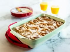 a pan filled with cinnamon rolls on top of a table next to two glasses of orange juice