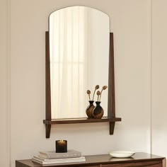 a mirror sitting on top of a wooden dresser next to a vase filled with flowers