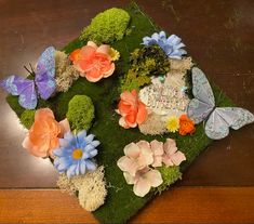 an arrangement of flowers, butterflies and moss on a wooden table with a sign that says happy birthday