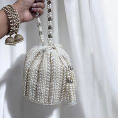 Introducing our exquisite Bridal Potli Bag in Ivory, a perfect accessory for your wedding day. Crafted from luxurious raw silk, this potli bag embodies elegance and sophistication. The delicate beadwork and sparkling crystal embellishments adorn the bag, adding a touch of opulence and grace. The bag features a stunning handmade handle, intricately embellished with beads and crystals, offering both beauty and functionality. Designed to complement your bridal attire, this potli bag is the ideal ch White Hand Embellished Party Bag, Elegant Beaded Party Pouch, Festive Elegant Beaded Potli Bag, White Handwork Clutch For Party, White Embellished Clutch For Party, White Clutch With Handwork For Party, Cream Pearl Evening Bag For Wedding, Rectangular Beaded Potli Bag For Wedding, White Hand Embellished Clutch