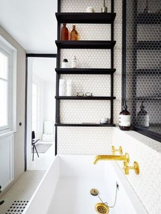 a white bath tub sitting under a window next to a shelf with bottles on it