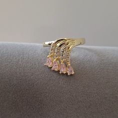 a gold ring with three pink stones on the front and side, sitting on top of a gray surface