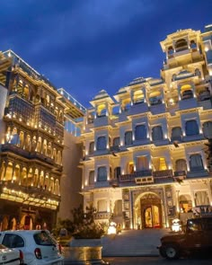 the hotel is lit up at night with cars parked in front