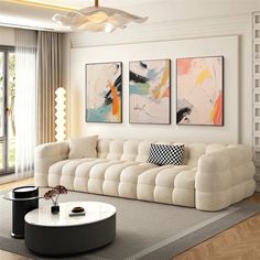 a living room with white furniture and paintings on the wall above it's couch