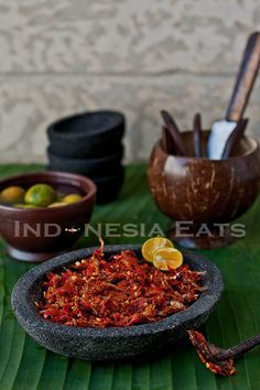 a bowl filled with food sitting on top of a green leaf covered table next to bowls and utensils