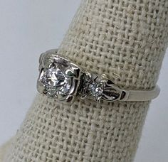 a white gold ring with three diamonds on the side, sitting on top of a burlock