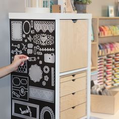 a person is drawing on the side of a black and white cabinet in a craft shop