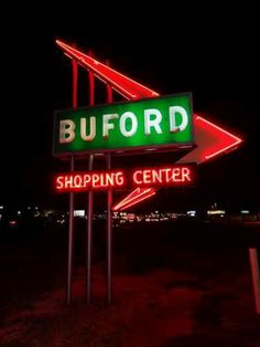 a neon sign that says buford shopping center in front of a parking lot at night