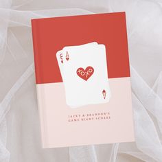 a red and white book with a playing card in the shape of a heart on it