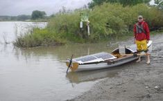 a man standing next to a small boat on top of a body of muddy water