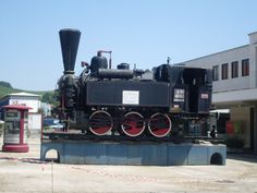 an old fashioned steam engine on display in front of a building with red and black wheels