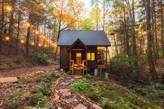 a small cabin in the woods surrounded by trees with lights hanging from it's roof