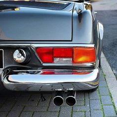 the rear end of a black car parked on a brick road