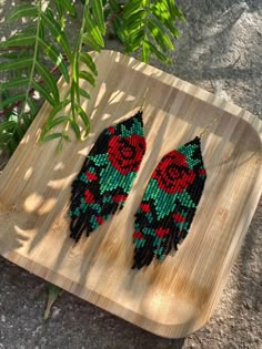 two pairs of beaded earrings sitting on top of a wooden tray next to a plant