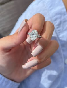 a woman's hand holding a ring with a diamond on it and her nails in the foreground