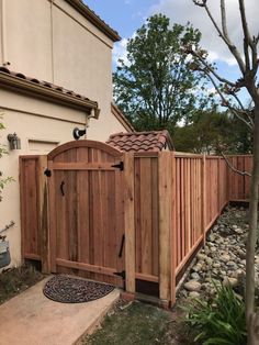 a wooden gate in front of a house next to a rock garden and small tree