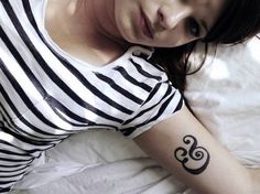 a woman laying on top of a bed wearing a black and white shirt with an om symbol tattooed on her arm