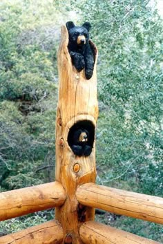 two black bears sitting on top of a wooden log structure with trees in the background