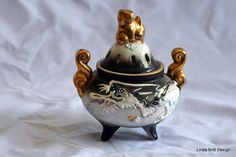 a black and white vase with gold decorations on it's top sitting on a white sheet