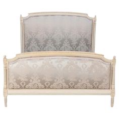 an antique style bed with white and beige upholstered headboard