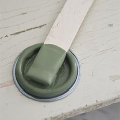 a green paint brush sitting on top of a white wooden table next to a round object