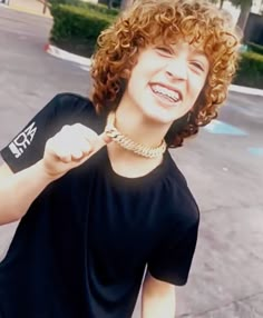 a woman with curly hair is smiling and pointing to the side while wearing a black t - shirt