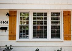 two windows with wooden shutters on the side of a white house in front of a mailbox