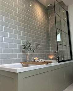 a bathroom with grey tiles and a white bathtub next to a window filled with candles