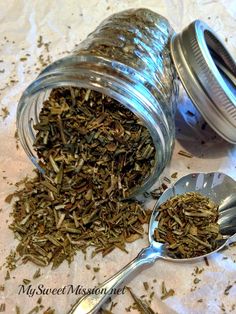 a jar filled with dried herbs next to two spoons on top of a table