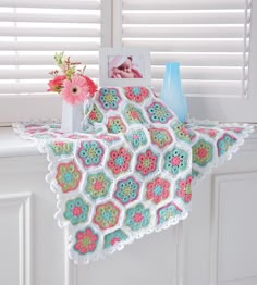 a crocheted blanket hanging on the side of a window sill with flowers