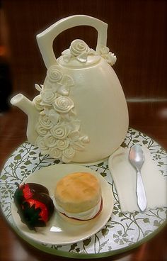 a white tea pot sitting on top of a table next to a plate with cake